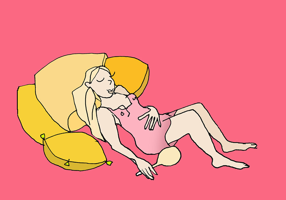 Frau liegt im Bett mit vielen Kissen und einer Hand auf ihrem Bauch und einem Taschenspiegel in der anderen Hand