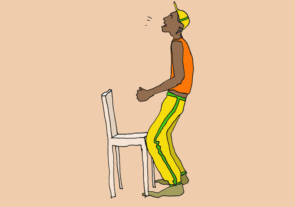 A man stands in front of a chair with his knees bent. He breathes out through the mouth and swings his pelvis forward.