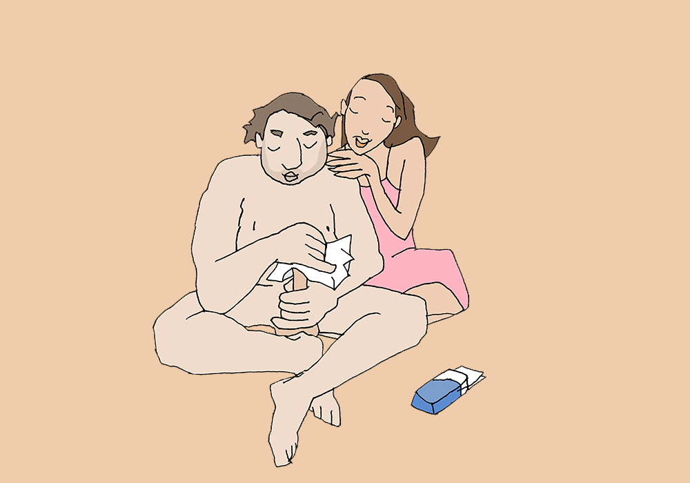 A naked man wipes his penis with a kleenex. A woman is sitting behind him putting her hands on his shoulder.
